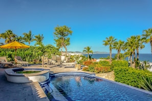 A pool area with lounge chairs and a view of the ocean.