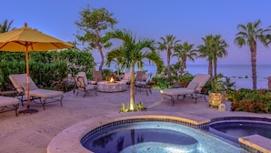 A pool area with lounge chairs, a fire pit, and a view of the ocean.