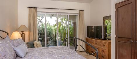 Ein Schlafzimmer mit einem Bett, einem Fernseher, einem Schminktisch und einer Glasschiebetür, die auf einen Balkon führt.