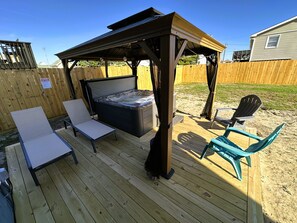 Una terraza de madera con un jacuzzi, dos sillones de relax y una zona de estar cubierta.