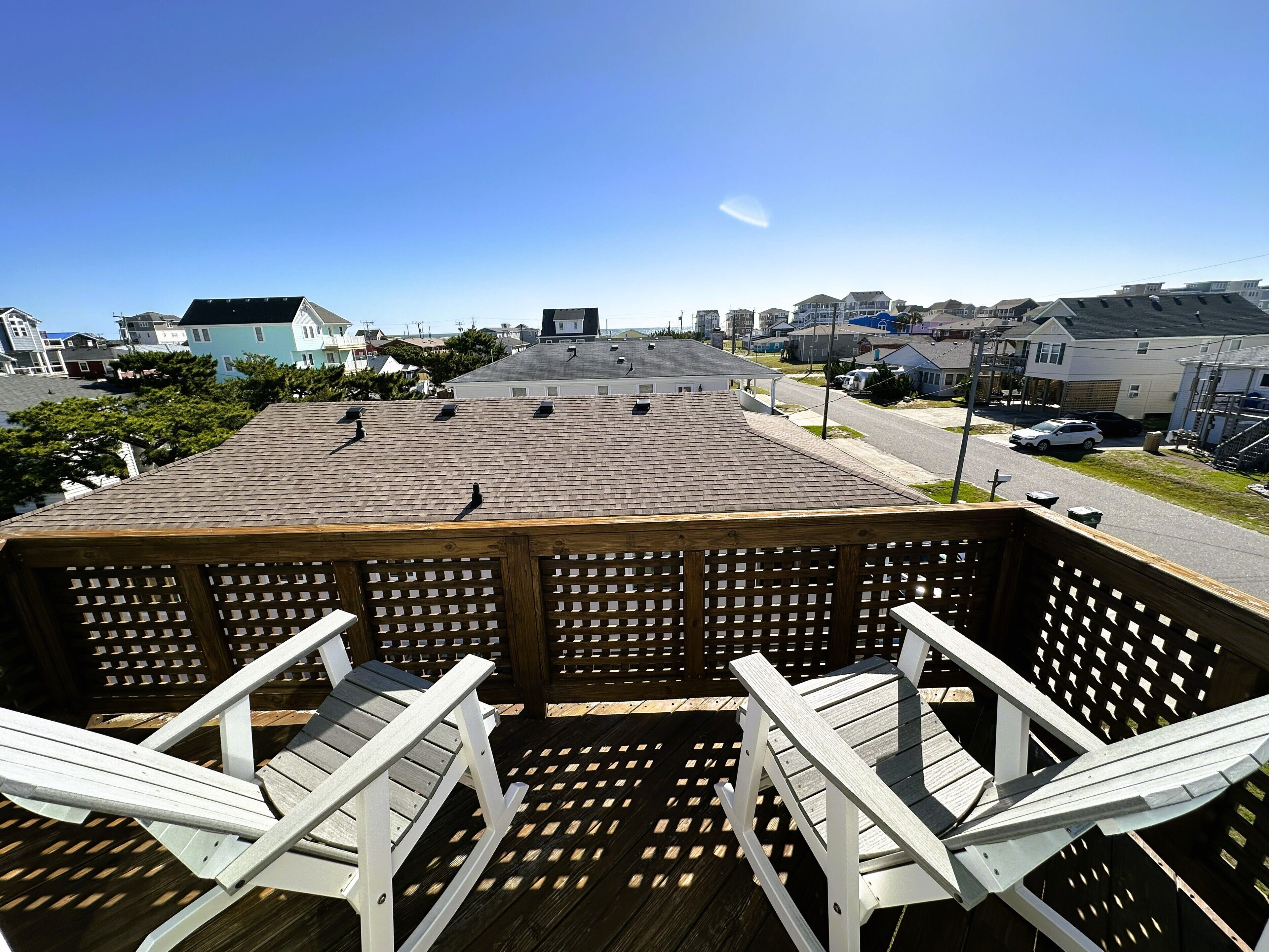 Um terraço com cadeiras Adirondack, vista clara do bairro e um edifício com telhado inclinado.