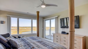 Ein Schlafzimmer mit einem großen Bett, einem Deckenventilator, einem Fernseher und Blick auf den Strand.