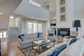 A spacious living room with a high ceiling, a staircase, and a balcony.