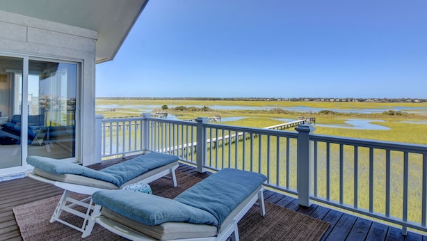 Ein Balkon mit zwei Loungestühlen, einer Glastür und Blick auf eine sumpfige Landschaft.