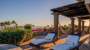 A beachside lounge with two sun loungers, a hammock, and a view of the ocean.