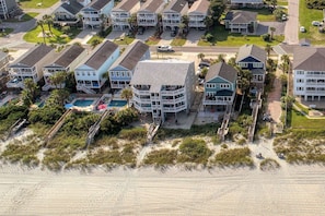 Un quartier résidentiel situé sur la côte, avec des propriétés donnant sur la plage, notamment un immeuble à plusieurs étages doté de balcons et d’une piscine.