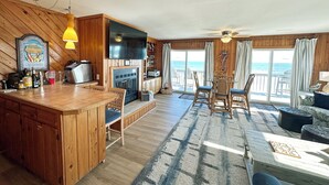 A spacious living area with a wooden interior, a fireplace, a television, and a view of the ocean through large windows. - SN9241- Beautiful Oceanfront Home with Great Ocean Views and Dog Friendly! (Nags Head)