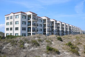 A multi-story residential building with balconies, located on a sandy terrain with sparse vegetation. - DR 2409 – Enjoy the pool, tennis and the beach from this oceanfront condo (Wrightsville Beach)