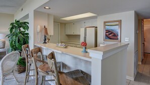 Una cocina moderna con armarios blancos, una isla central y un comedor con sillas de mimbre.