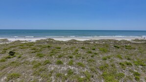 Un paisaje costero con una playa, dunas cubiertas de hierba y un cielo azul despejado.