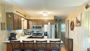 Una cocina con armarios de madera, una isla central con taburetes de bar, un microondas, una estufa y un refrigerador.