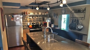 A modern kitchen with stainless steel appliances, a large island with a sink, and various utensils hanging on the wall.