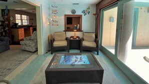 A cozy living room with a glass coffee table, two cushioned chairs, a fireplace, and a large sliding glass door to the outside.