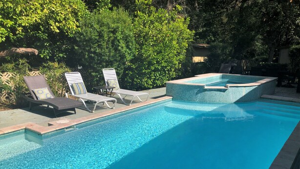 A swimming pool with clear water, surrounded by lounge chairs and a hot tub.