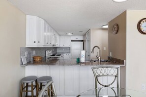 A modern kitchen with white cabinets, a stainless steel sink, and a glass island with stools. - *20% Off New Summer 2026 Bookings* (Garden City)