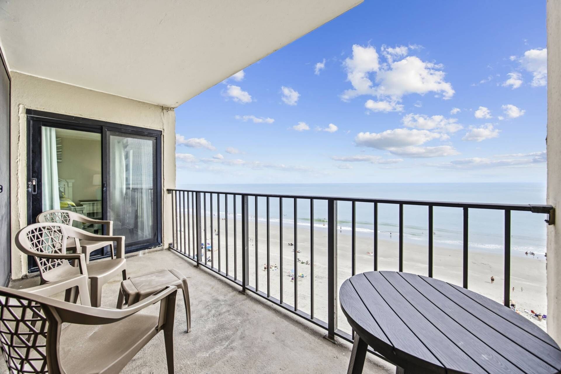 A balcony with a view of the beach, a table, and two chairs.