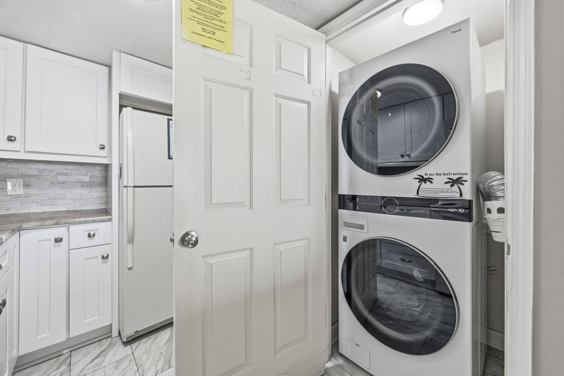 A laundry room with two stacked front-loading washing machines, a white door, and a tiled backsplash.