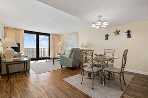 Relax in a spacious living room with a sofa, armchairs, and dining table, offering a view of the outdoors.
