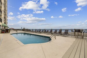 Relax by the ocean-view pool, surrounded by lounge chairs and a low railing.