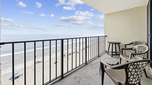 Ein Balkon mit Blick auf den Strand, ein Tisch, zwei Stühle und ein kleiner runder Beistelltisch.