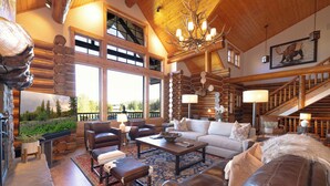 A spacious living area with a fireplace, leather furniture, and a large window overlooking a garden. - Salmonfly Lodge Remodeled Teton Springs Log Cabin in Victor w/ Hot Tub & A/C (Victor)