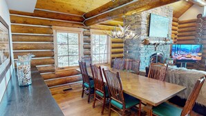 A log cabin interior with a dining table, chairs, a stone fireplace, and a mounted deer head. - Salmonfly Lodge Remodeled Teton Springs Log Cabin in Victor w/ Hot Tub & A/C (Victor)