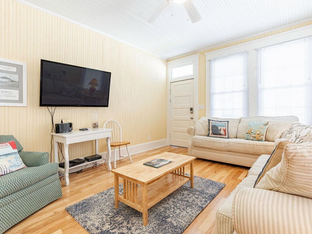 Een woonkamer met een televisie, een wit bureau, een groene bank en een beige bank.
