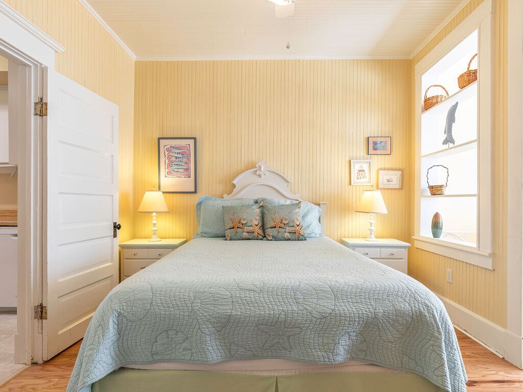 A bedroom with a bed, two bedside tables, a window with baskets, and a door.