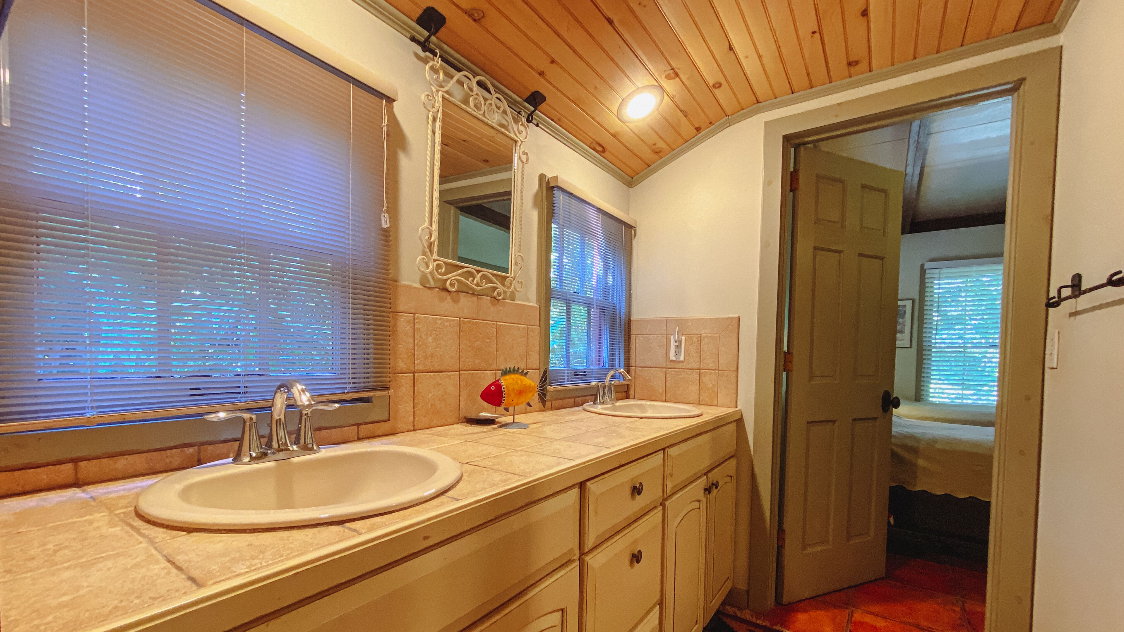 A bathroom with two sinks, a mirror, and a door leading to another room.