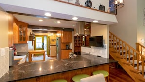 A modern kitchen with a marble countertop, wooden cabinets, and a built-in stove. There is a bar area with stools and a staircase leading to an upper level. - Wine to Water - Family Adventure on Keuka Lake Awaits! (Hammondsport)