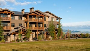 Un chalet à plusieurs étages, doté d’une façade en pierre, de balcons en bois et offrant une vue sur les montagnes en arrière-plan.
