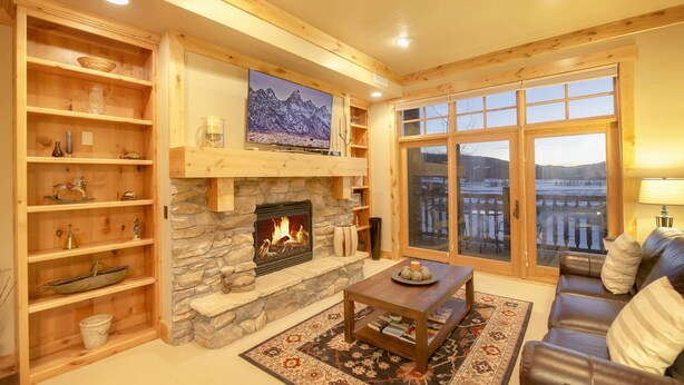 Un salon chaleureux avec une cheminée en pierre, des étagères en bois, une grande fenêtre offrant une belle vue et un canapé en cuir.