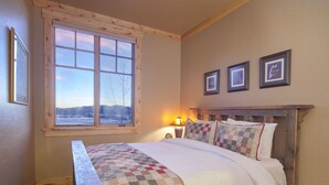 Une chambre à coucher avec un lit en bois, une courtepointe, une fenêtre donnant sur un paysage enneigé et trois tableaux encadrés accrochés au mur.