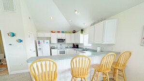 Una cocina moderna con armarios blancos, una isla central con taburetes de bar y un microondas sobre la isla.