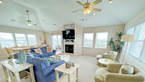 Un salón amplio con un sofá azul, sillones beige, una chimenea y ventanas grandes que ofrecen una vista.