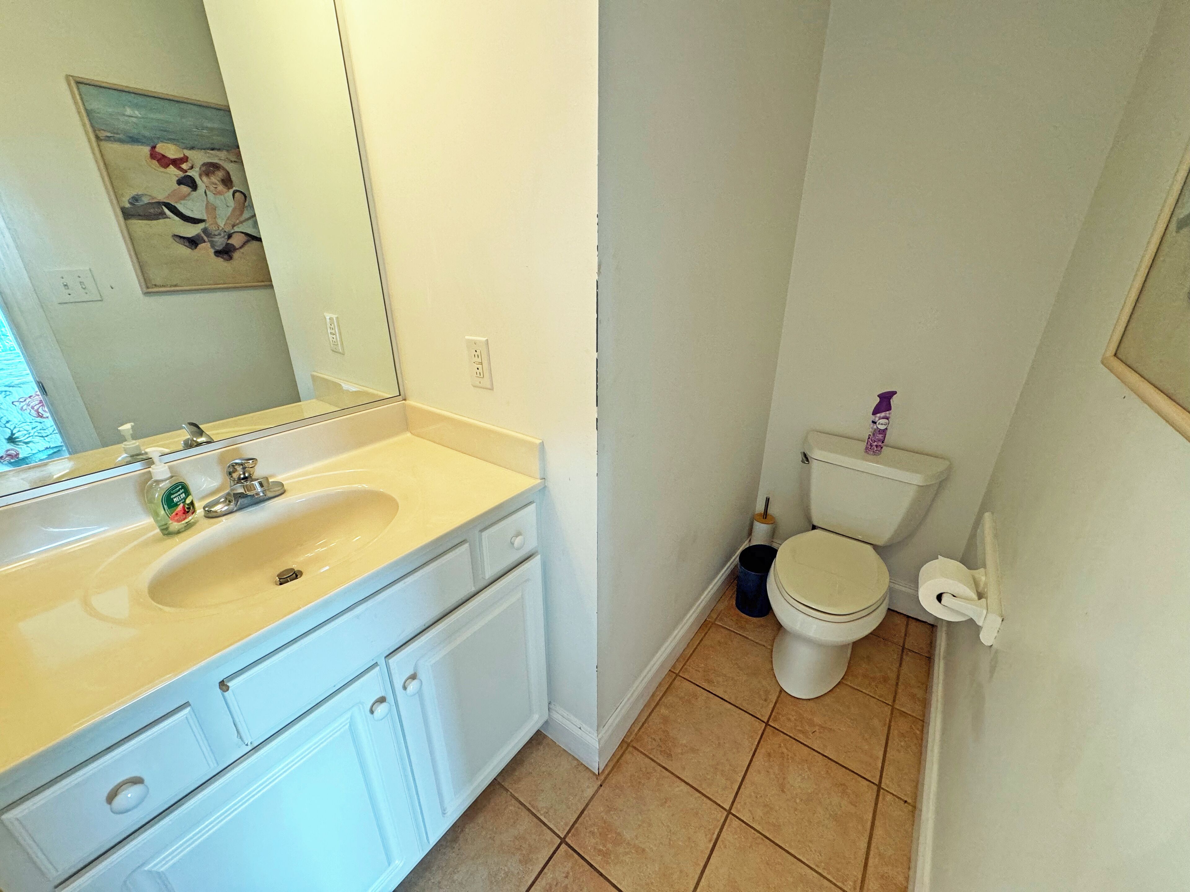 A bathroom with a sink, mirror, toilet, and a trash bin.