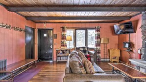 A cozy cabin interior with a wooden ceiling, a sofa with patterned cushions, a television mounted on the wall, and a stone fireplace. - Deck + Fire Pit: Family Cabin in Bessemer (Bessemer)