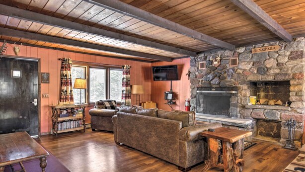 A cozy living room with a stone fireplace, wooden ceiling beams, a television, and a sofa. - Deck + Fire Pit: Family Cabin in Bessemer (Bessemer)