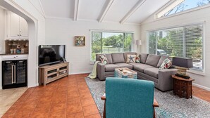 Ein Wohnzimmer mit Ecksofa, Fernseher und Küchenzeile, inklusive Kühlschrank und Schränken.