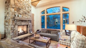 A cozy living room with a stone fireplace, comfortable seating, and large windows offering a view of the outdoors. - PETRA DOMUS- SKI PASSES! Luxury Stone House w/ Hot Tub, Guest House (Mountain Village)