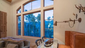 A cozy room with a large window, a dining table with a pine cone centerpiece, and a leather sofa. - PETRA DOMUS- SKI PASSES! Luxury Stone House w/ Hot Tub, Guest House (Mountain Village)