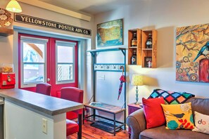 A room with a red door, a map on the wall, a wooden shelf with bottles, and a couch with colorful pillows.