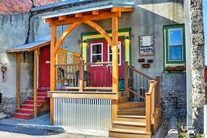 A colorful building with a wooden porch, a red door, and a staircase leading to the entrance.