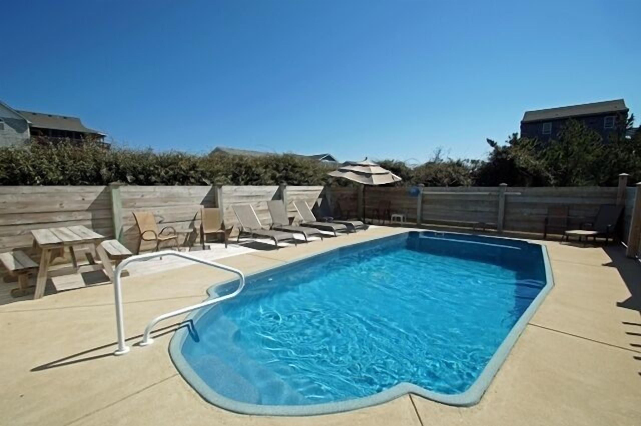 A rectangular swimming pool with a metal ladder, surrounded by lounge chairs and a wooden deck.