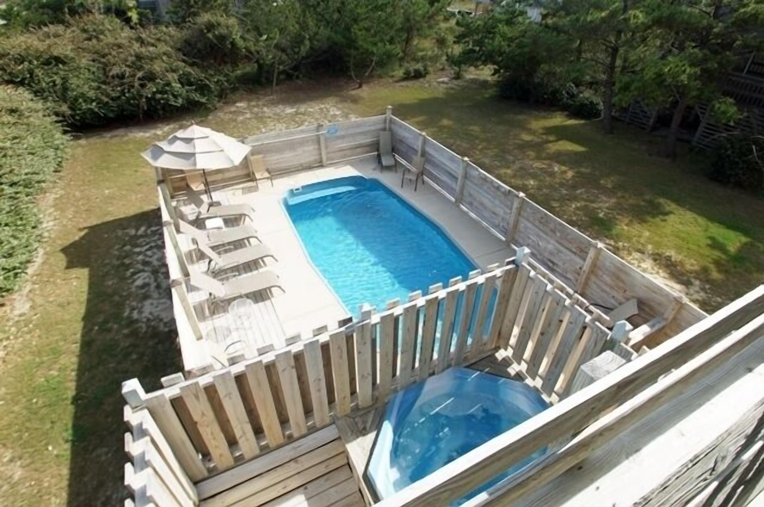 Un patio trasero con piscina, sillas de deck y valla de madera.