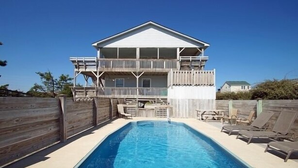 Une maison à deux étages avec une piscine, une terrasse en bois et du mobilier d’extérieur.
