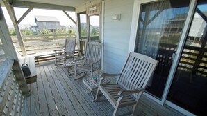 Un espace extérieur abrité doté d’une terrasse en bois, de trois chaises en bois et d’une porte-fenêtre coulissante.