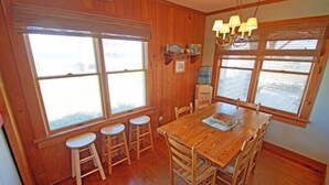 Une salle à manger aux murs lambrés, avec une table en bois et quatre tabourets.
