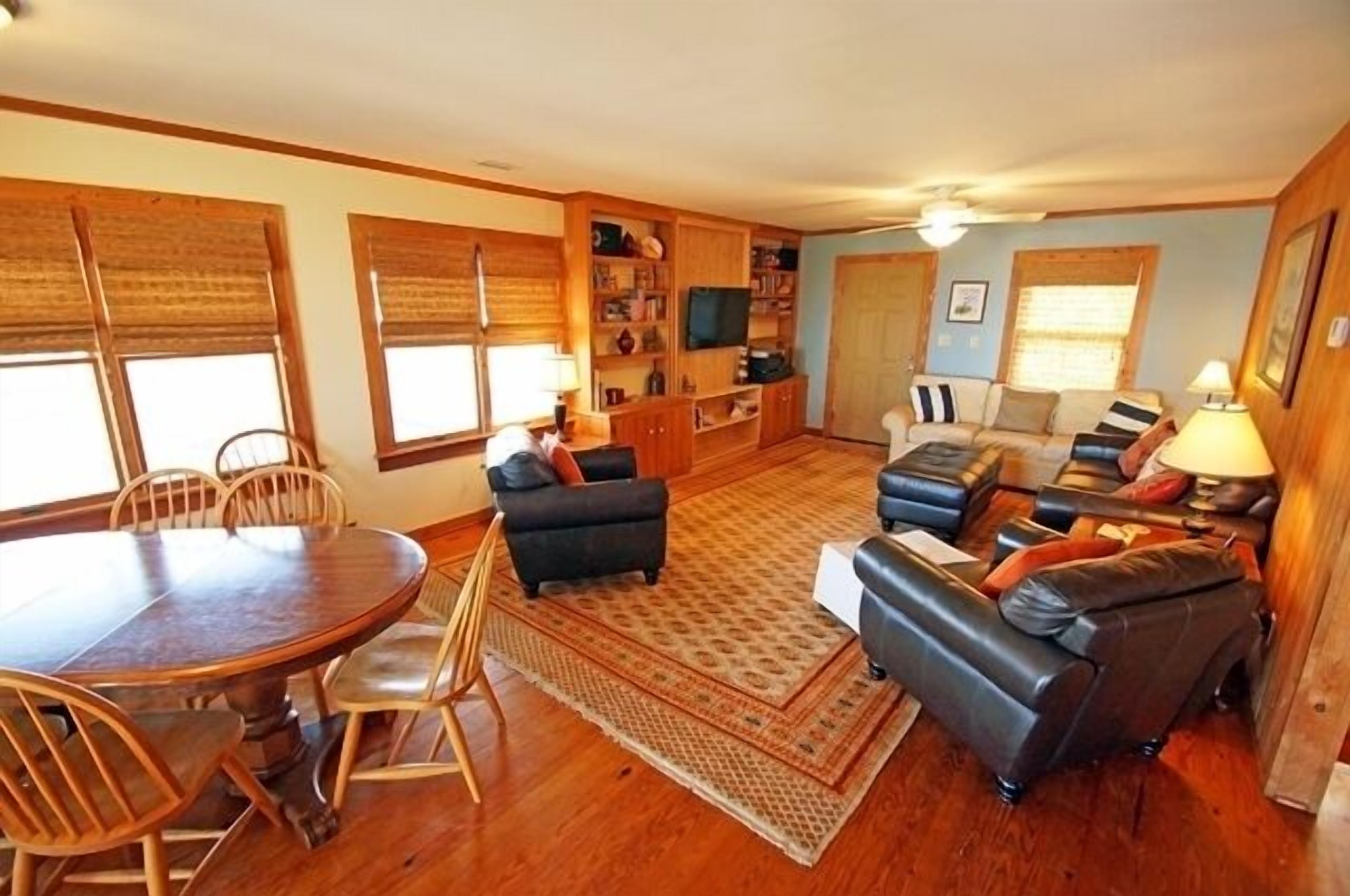 A spacious living room with a wooden dining table, comfortable seating, and a television.