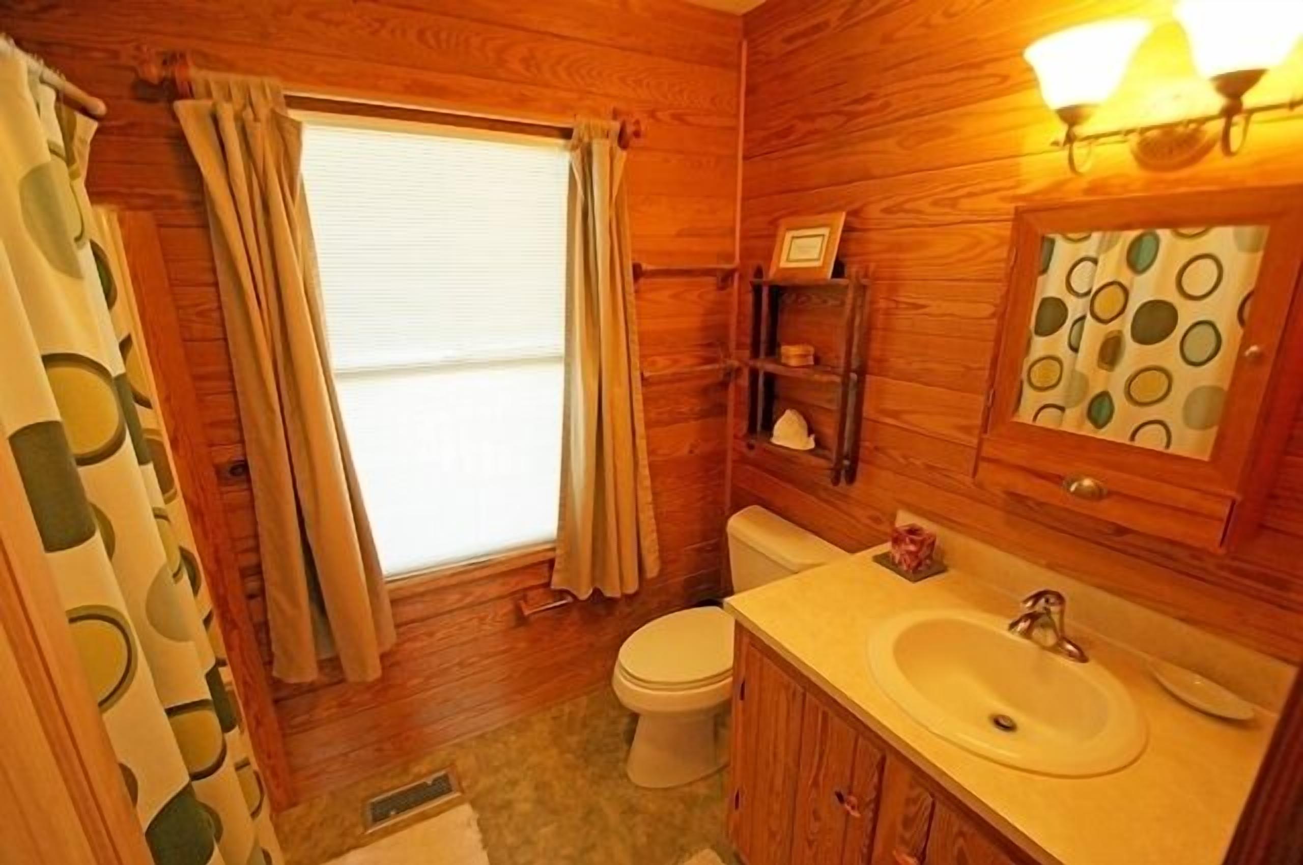 A wooden-paneled bathroom with a toilet, sink, and a window with curtains.